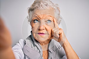 Senior beautiful grey-haired woman making selfie by camera over isolated white background serious face thinking about question,