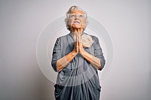 Senior beautiful grey-haired woman wearing casual dress standing over white background begging and praying with hands together