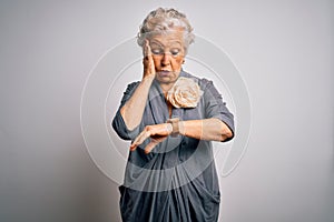 Senior beautiful grey-haired woman wearing casual dress standing over white background Looking at the watch time worried, afraid