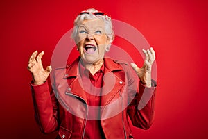 Senior beautiful grey-haired woman wearing casual red jacket and sunglasses crazy and mad shouting and yelling with aggressive