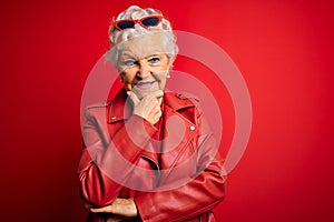 Senior beautiful grey-haired woman wearing casual red jacket and sunglasses looking confident at the camera smiling with crossed