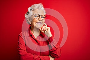 Senior beautiful grey-haired woman wearing casual shirt and glasses over red background looking confident at the camera with smile