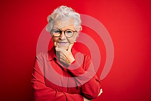 Senior beautiful grey-haired woman wearing casual shirt and glasses over red background looking confident at the camera smiling