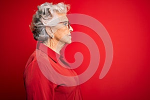 Senior beautiful grey-haired woman wearing casual shirt and glasses over red background looking to side, relax profile pose with