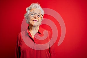 Senior beautiful grey-haired woman wearing casual shirt and glasses over red background Relaxed with serious expression on face