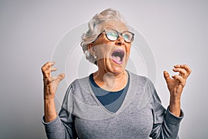 Senior beautiful grey-haired woman wearing casual sweater and glasses over white background crazy and mad shouting and yelling