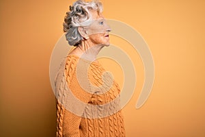 Senior beautiful grey-haired woman wearing casual sweater over isolated yellow background looking to side, relax profile pose with