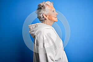 Senior beautiful sporty woman wearing white sweatshirt over isolated blue background looking to side, relax profile pose with