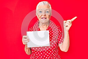 Senior beautiful woman with blue eyes and grey hair holding blank empty banner smiling happy pointing with hand and finger to the