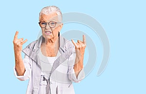Senior beautiful woman with blue eyes and grey hair wearing casual clothes and glasses shouting with crazy expression doing rock