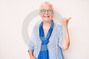 Senior beautiful woman with blue eyes and grey hair wearing casual sweater and scarf pointing thumb up to the side smiling happy