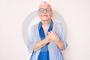 Senior beautiful woman with blue eyes and grey hair wearing casual sweater and scarf smiling with hands on chest, eyes closed with