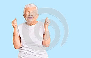 Senior beautiful woman with blue eyes and grey hair wearing casual white tshirt excited for success with arms raised and eyes