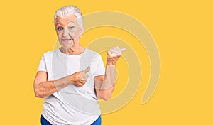 Senior beautiful woman with blue eyes and grey hair wearing casual white tshirt pointing to the back behind with hand and thumbs