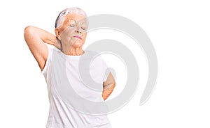 Senior beautiful woman with blue eyes and grey hair wearing casual white tshirt suffering of neck ache injury, touching neck with