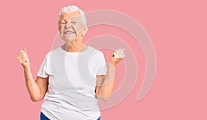 Senior beautiful woman with blue eyes and grey hair wearing casual white tshirt very happy and excited doing winner gesture with