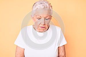 Senior beautiful woman with blue eyes and grey hair wearing classic white tshirt over yellow background with hand on stomach