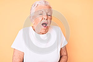 Senior beautiful woman with blue eyes and grey hair wearing classic white tshirt over yellow background with hand on stomach
