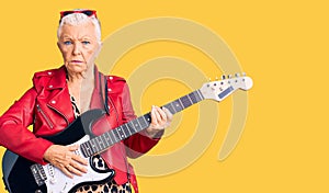 Senior beautiful woman with blue eyes and grey hair wearing a modern look playing electric guitar depressed and worry for