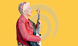 Senior beautiful woman with blue eyes and grey hair wearing a modern look playing electric guitar looking to side, relax profile