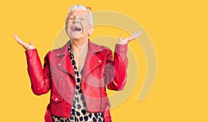 Senior beautiful woman with blue eyes and grey hair wearing a modern style with a red leather jacket celebrating mad and crazy for