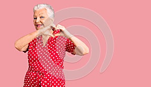 Senior beautiful woman with blue eyes and grey hair wearing a red summer dress smiling in love doing heart symbol shape with hands