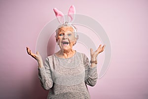 Senior beautiful woman wearing bunny ears standing over isolated pink background celebrating mad and crazy for success with arms