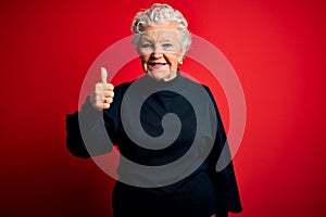 Senior beautiful woman wearing casual sweater standing over isolated red background doing happy thumbs up gesture with hand