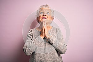 Senior beautiful woman wearing casual t-shirt standing over isolated pink background begging and praying with hands together with