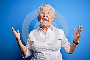 Senior beautiful woman wearing elegant shirt standing over isolated blue background crazy and mad shouting and yelling with