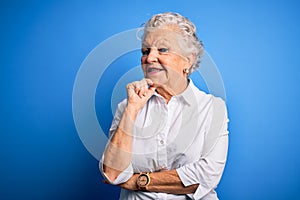 Senior beautiful woman wearing elegant shirt standing over isolated blue background looking confident at the camera with smile