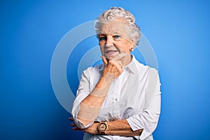 Senior beautiful woman wearing elegant shirt standing over isolated blue background looking confident at the camera smiling with