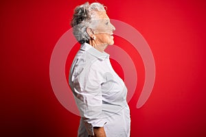 Senior beautiful woman wearing elegant shirt standing over isolated red background looking to side, relax profile pose with