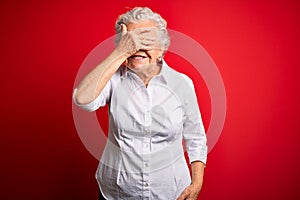 Senior beautiful woman wearing elegant shirt standing over isolated red background smiling and laughing with hand on face covering