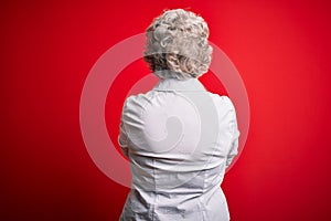 Senior beautiful woman wearing elegant shirt standing over isolated red background standing backwards looking away with crossed