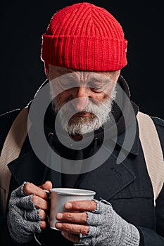 Senior beggar male holding mug of hot tea for warming up