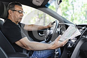 Senior behind the steering wheel looking at map for directions