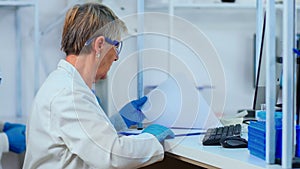 Senior biochemist typing and looking on pc analysing medical reports