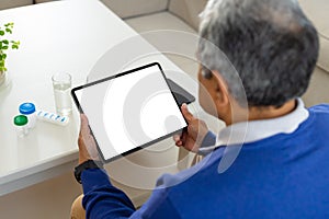 Senior biracial man sitting at table with medicine bottles using tablet, copy space on screen