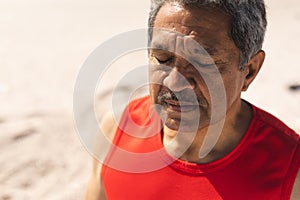 Senior biracial retired man meditating with eyes closed at beach on sunny day