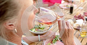 Senior biracial woman enjoys a glass of wine at an outdoor dining table