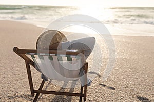 Senior biracial woman wearing hat sitting on folding chair relaxing at beach during sunset