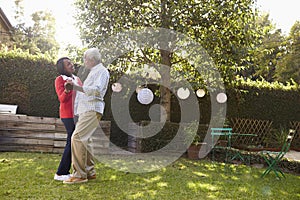 Senior black couple dance in their back garden, full length