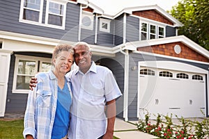 Senior black couple standing outside a large suburban house