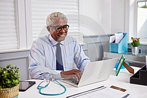 Senior black male doctor at work using laptop in an office