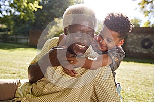 Senior black man sitting on grass, embraced by his grandson