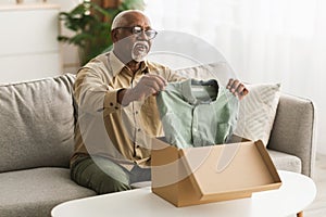 Senior Black Man Unpacking Box Looking At Shirt At Home