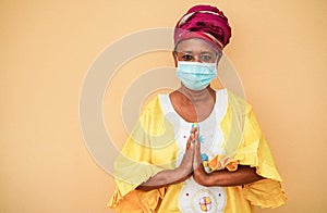 Senior black woman holding hands in prayer position wearing traditional african dress - Social distance concept