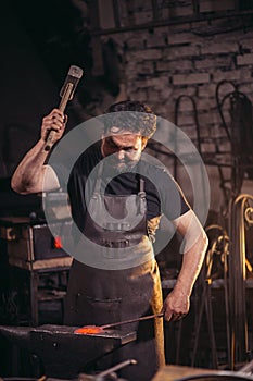 Senior blacksmith forging molten metal on the anvil in smithy.