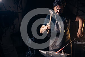 Senior blacksmith forging molten metal on the anvil in smithy.